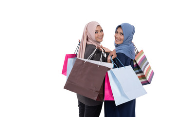 Asian young and old veiled women looking back while carrying some shopping bags at isolated background