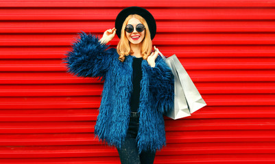 Portrait stylish smiling woman with shopping bags wearing blue faux fur coat, black round hat and...