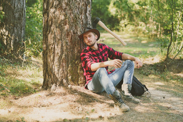 Woodcutter with axe in the summer forest. Illegal logging continues today. Lumberjack standing with axe on forest background.