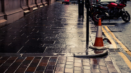 A lone traffic cone on a wet sidewalk