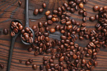 Spoon with roasted coffee beans on wooden background, top view