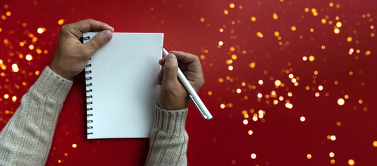 Mans right hand holds white pen and left hand holds a white papered blank notebook, view from the top, red background, banner