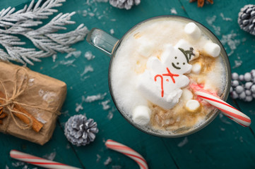 Christmas composition, mug with hot chocolate with melted snowman marshmallows and caramel. horizontal frame over green background
