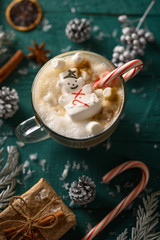 Christmas and New Year. Marshmallow snowman in hot latte in a mug. Vertical composition on a green background.