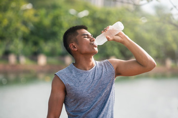 Portrait of healthy man with fit body holding bottle of refreshing water, resting after workout or running. Male with a drink after outdoor training.