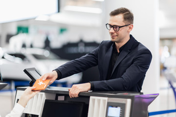 Side view of handsome man wearing glasses giving passport to staff at check in desk at airport