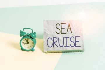 Handwriting text writing Sea Cruise. Conceptual photo a voyage on a ship or boat taken for pleasure or as a vacation Mini size alarm clock beside a Paper sheet placed tilted on pastel backdrop