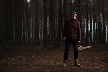 Fototapeta premium Lumberman working with chainsaw in the forest. Strong lumberjack with the chainsow in the forest.Stylish lumberman getting ready for work. Lifestyle.
