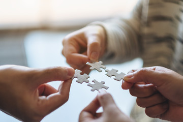 Closeup image of many people holding and putting a piece of white jigsaw puzzle together