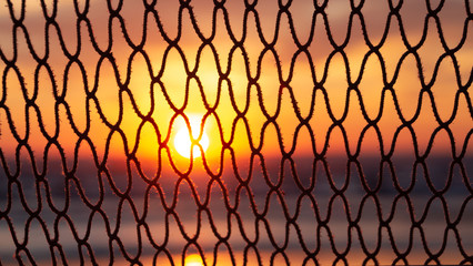 colorful blurred ocean sunrise seen through a fishing net on sunny morning at Rivazzurra (Rimini/Italy) beach