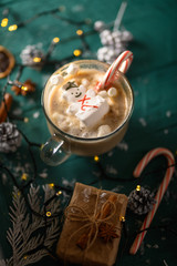 Christmas and New Year. Marshmallow snowman in hot latte in a mug. Vertical composition on a green background.