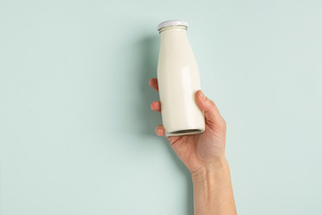Female hand holds milk or white milk drink in a glass bottle on white background. Healthy eating...