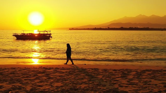 A Woman Walking At The Shore Under The Silhouette Of The Bright And Glowing Sunrise, Shinning Over The Ocean, Mountains, And Vessels In Tahiti Island - Wide Shot