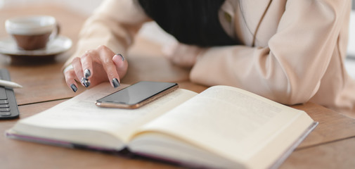 Close-up view of businesswoman using her smartphone while working on her project in comfortable workspace