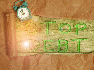 Writing note showing Stop Debt. Business concept for does not owning any money or things to any individual or companies Alarm clock and torn cardboard on a wooden classic table backdrop