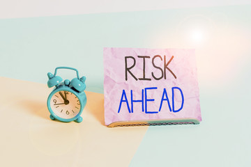 Handwriting text writing Risk Ahead. Conceptual photo A probability or threat of damage, injury liability and loss Mini size alarm clock beside a Paper sheet placed tilted on pastel backdrop