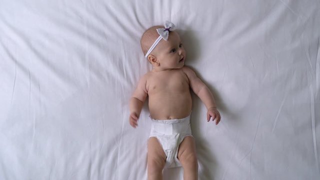 Active baby girl wearing comfortable soft diaper, lying on bed, moving legs