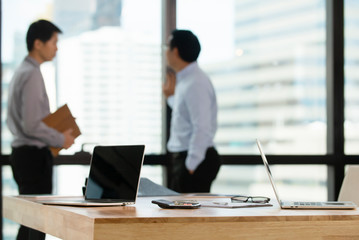 Laptop  computer on tables in meeting room with equipment in conference room blurred two bussiness man talking background  , teamwork business success concept