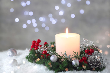 Burning candle with evergreen arrangment and christmas decoration,over gray with illuminaton background. 