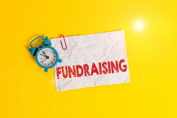 Text sign showing Fundraising. Business photo showcasing act of collecting or producing money for a particular purpose Metal alarm clock clip blank crushed note sheet colored background