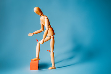 Joint pain concept. The wooden man holds his hands on sore red knee.