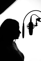 Silhouette of a girl with a studio microphone, Radio presenter, singer and blogger, voice acting for films. Strong, black and white photo. Vertical photo