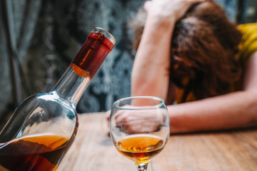 Drunk woman fell asleep at the table next to a bottle of liquor. Alcoholism concept