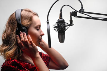 The singer sings in a recording studio, on the radio. In headphones, on a light background.
