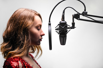 The singer sings in a recording studio, on the radio. In headphones, on a light background.