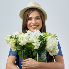 smiling woman holding white and green flowers in big glass vase.