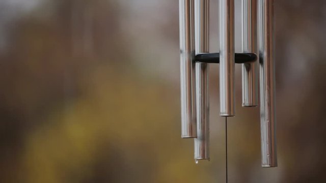 Rain drops splash and fall from a set of wind chimes with autumn colors in the background