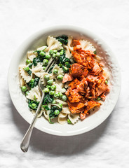 Farfalle pasta with green peas spinach cream sauce and roasted salmon on light background, top view