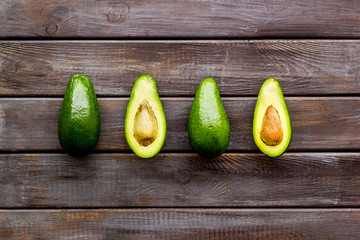 Avocado pattern - halfs of fruit - on dark wooden background top view copy space