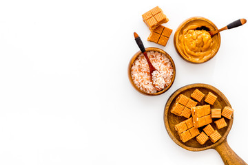 Cook salted caramel. Scoop with sweet cubes, melted caramel and salt on white background top view copy space