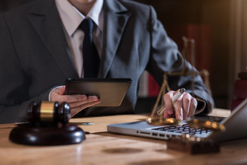Justice and law concept.Male judge in a courtroom the gavel, working with digital tablet computer on wood table.