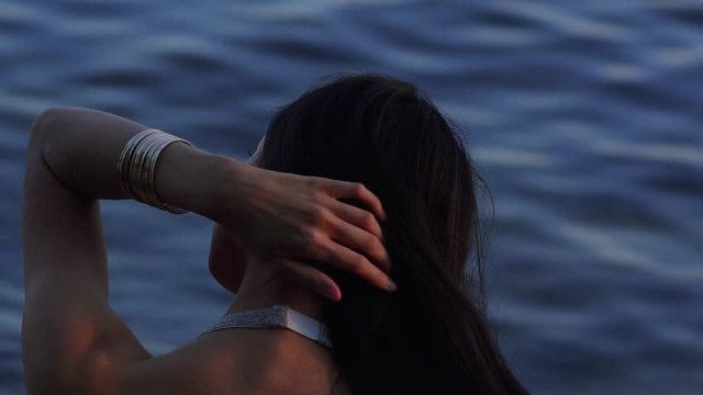 Close video of a woman back in a beautiful dress near water. Woman fixing her hair in slow motion.
