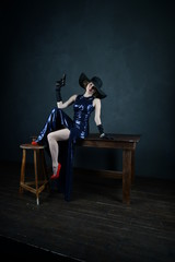 girl in a blue evening dress and in a black hat on a gray background with a gun