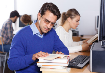 Fototapeta premium Serious student reading textbooks in computer class