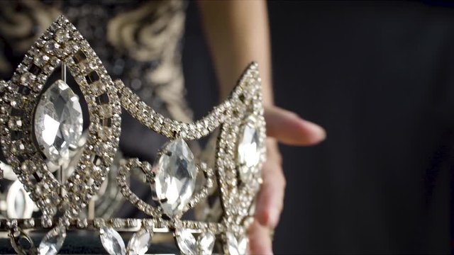 A beauty pageant winner takes her diamond crown and places it on her head while looking in a mirrior