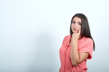 Fototapeta premium Attractive caucasian young woman keeping hand on cheek, thinking about issue isolated on white background in studio in fasion pink shirt . People sincere emotions, lifestyle concept.