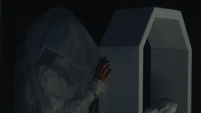 Gloomy look of a ghost bride behind a coffin with a veil covering her face. Dark environment