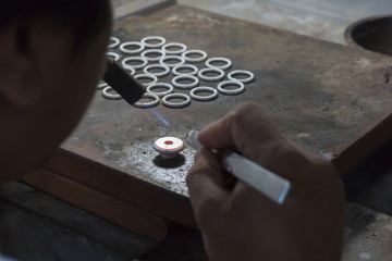 Close up of a men goldsmith working and shaping an unfinished ring with a tool at workbench in workshop.