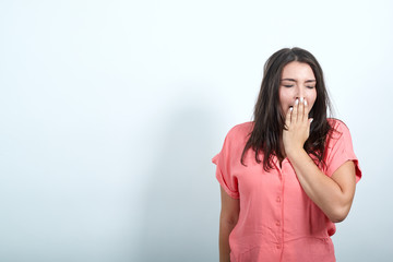 Fototapeta premium Attractive caucasian young woman in pink shirt keeping hand on mouth, yawning isolated on white background in studio. People sincere emotions, lifestyle concept.