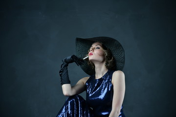 girl in a blue evening dress and a black hat with a cigarette