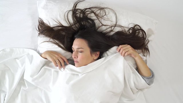 Image from above of woman waking up and getting shy in front of camera.