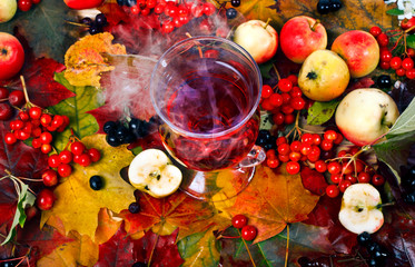 Mulled wine with vapour on a background of fallen autumn leaves, apples and berries. Top view....