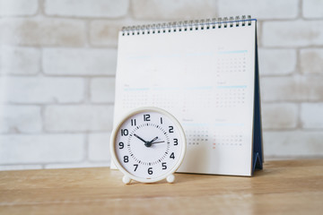 white analog clock with blurred calendar on wooden table