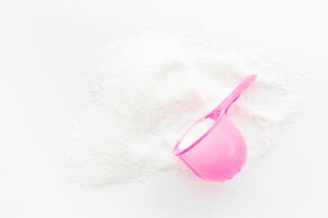 Washing powder in plastic spoon on white background top view