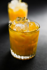 Two rocks glasses filled with ice cubes and orange juice on dark background, back side light
