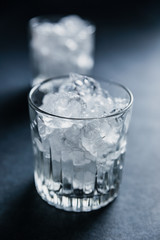 Two rocks glasses filled with ice cubes on dark background, back side light